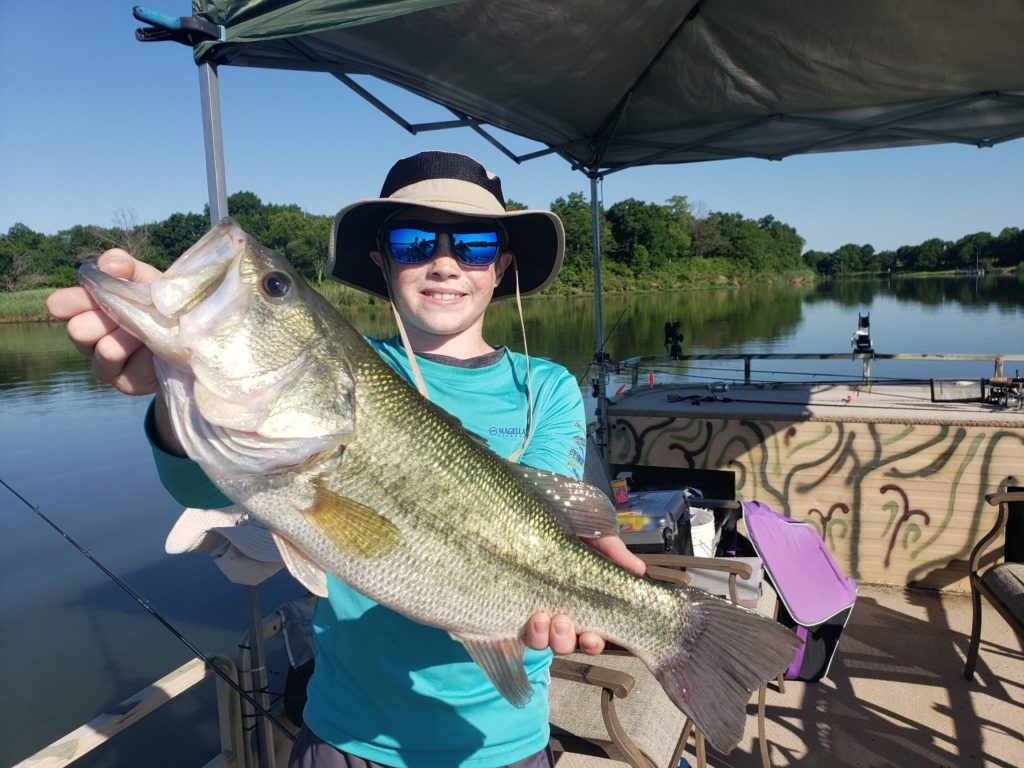 Small kid with sunglasses and hat holding a huge fish